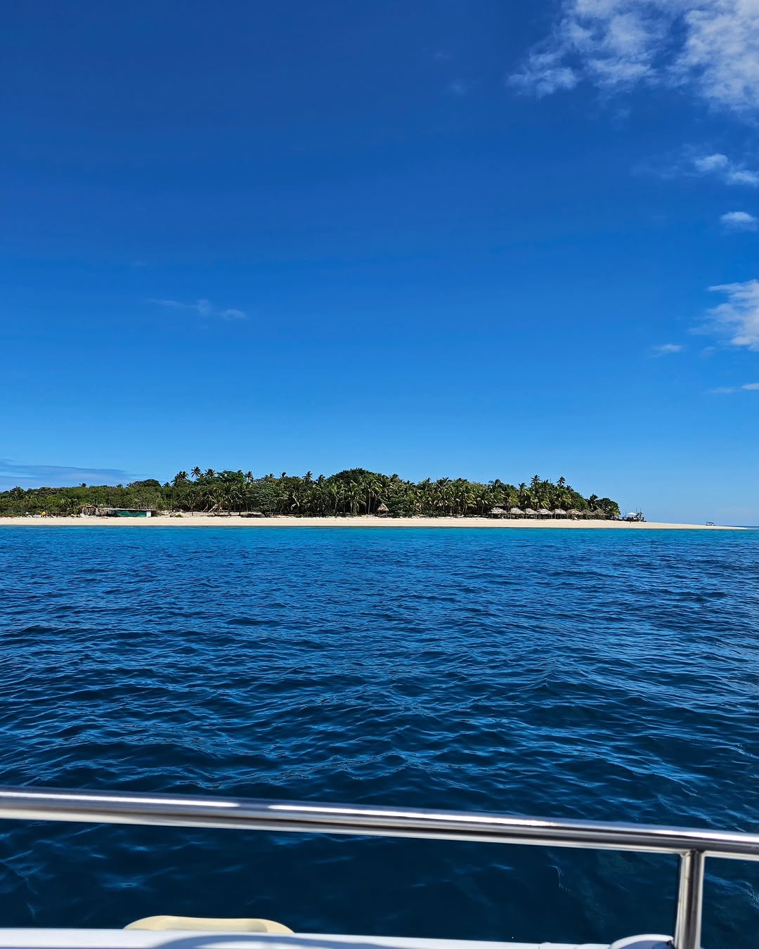 Palm island and white beach approached from the sea in Fiji